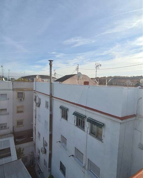 Vista de edificios de apartamentos blancos y tejados bajo un cielo azul con nubes finas.
