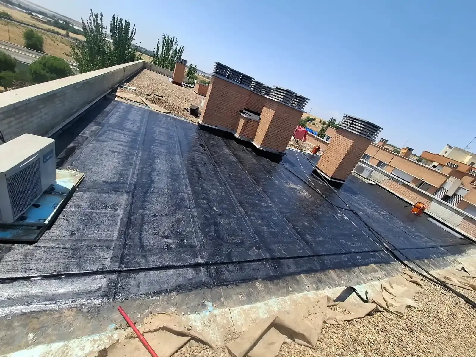Azotea plana con impermeabilización negra, varias chimeneas de ladrillo y un cielo azul despejado.