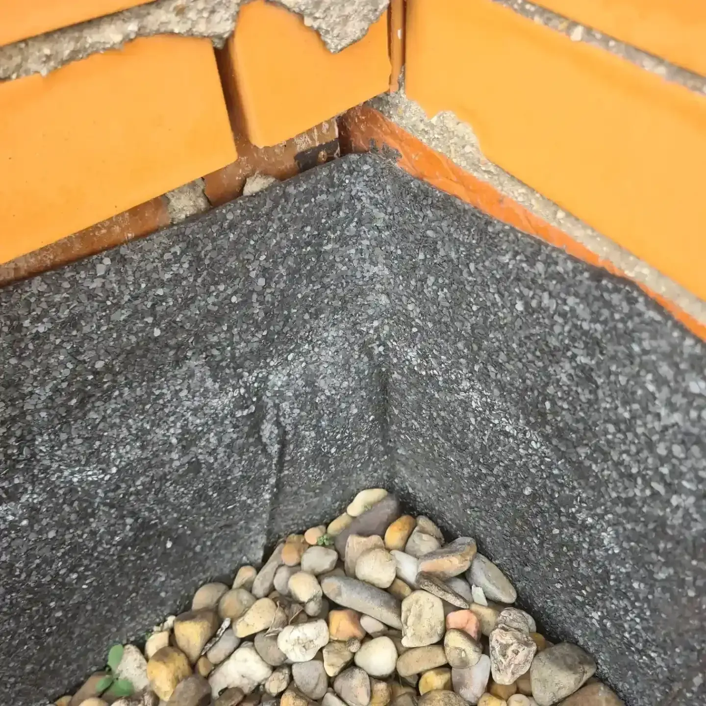 Primer plano de una jardinera de ladrillo en la esquina, con revestimiento negro y guijarros en la base.