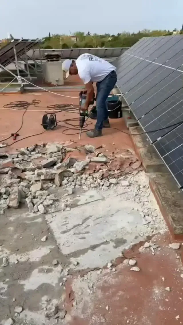 Un trabajador instala paneles solares en un tejado rojo dañado, con herramientas a su alrededor.