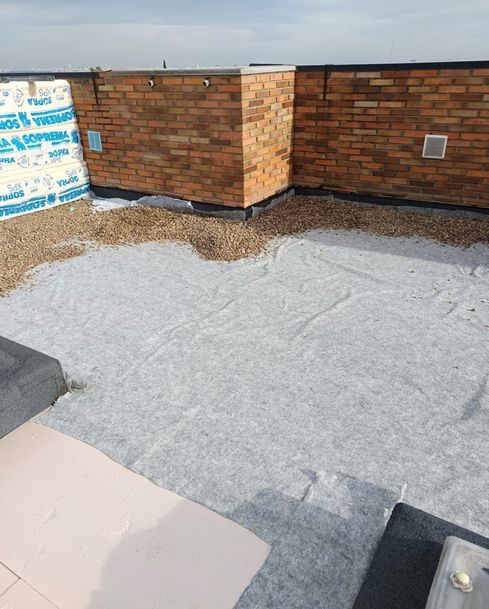 Azotea plana con muros de parapeto de ladrillo y una membrana impermeabilizante gris en construcción.