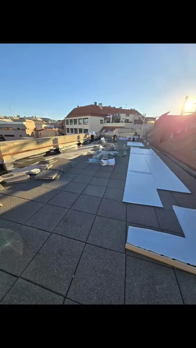 Azotea al atardecer con trabajadores, paneles de techo blancos y un edificio al fondo.
