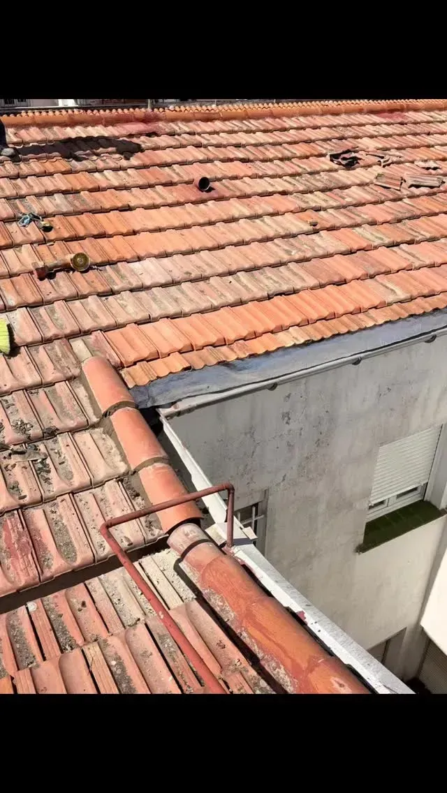 Tejas de terracota roja junto a una pared gris, con una tubería blanca que recorre el borde del tejado.