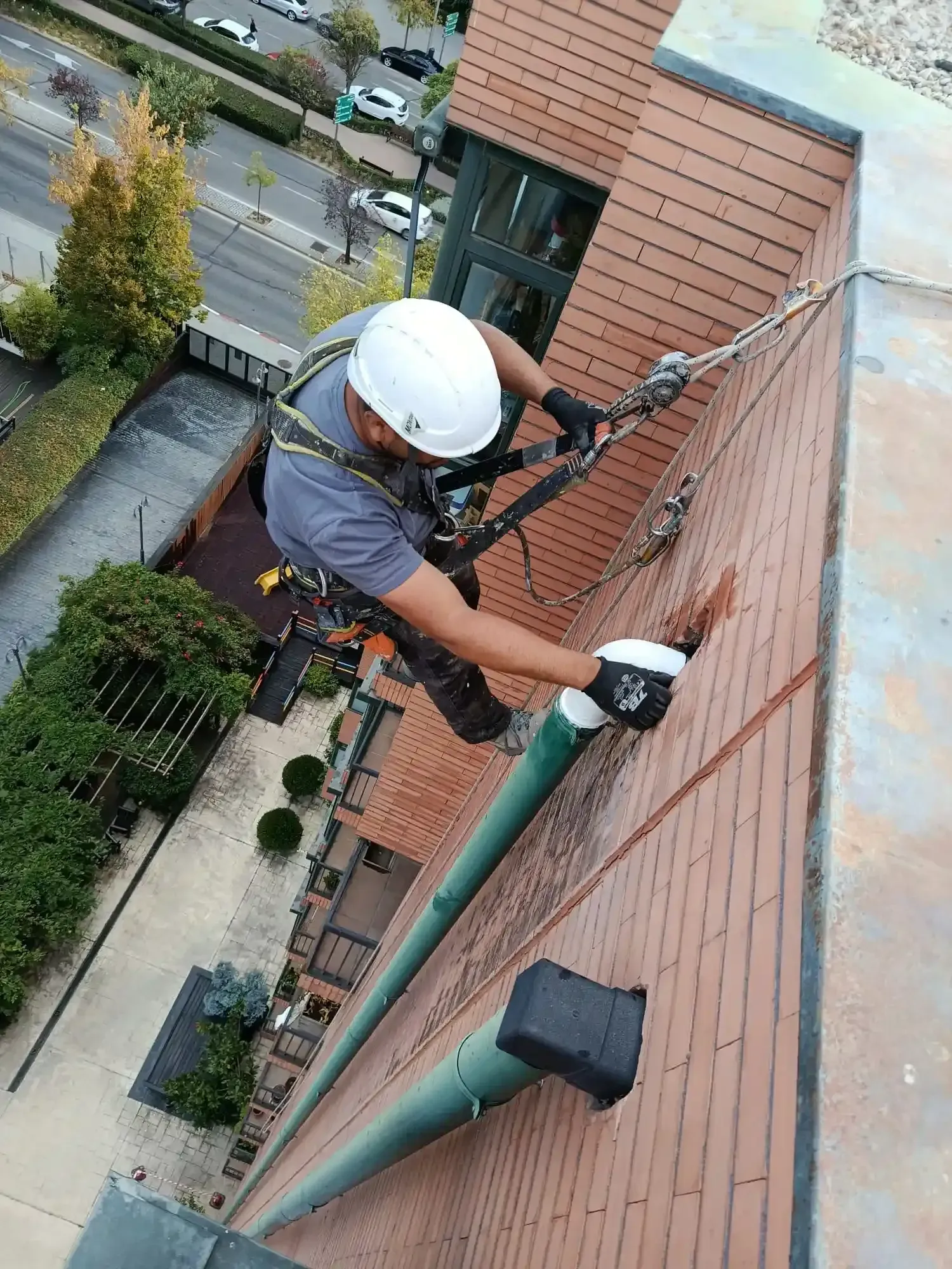 Trabajador con casco y arnés de seguridad en una pared de ladrillos durante trabajos de mantenimiento del edificio.