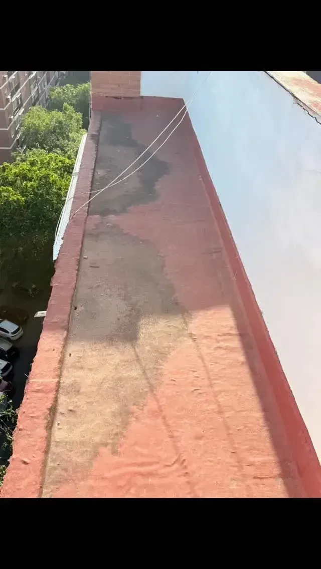 Pasarela en la azotea con suelo rojo, una pared blanca y vegetación debajo a la izquierda.