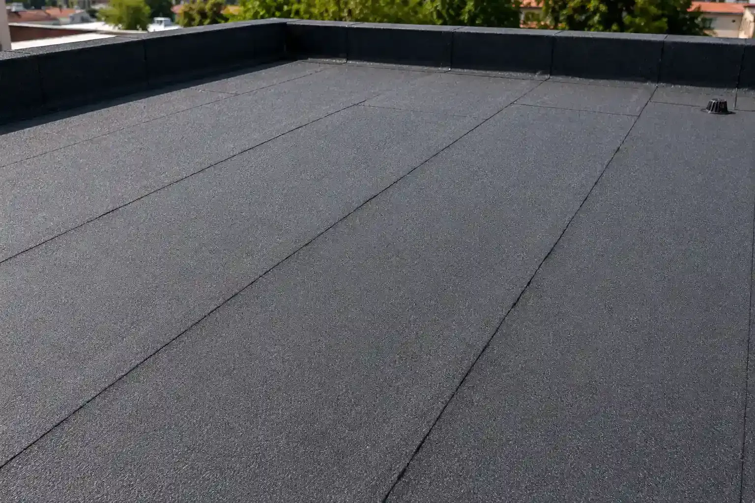 Techo plano gris con superficie de grava y muros de parapeto negros bajo la luz del día.