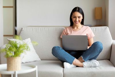 Eine Frau sitzt auf einem Sofa und benutzt einen Laptop.