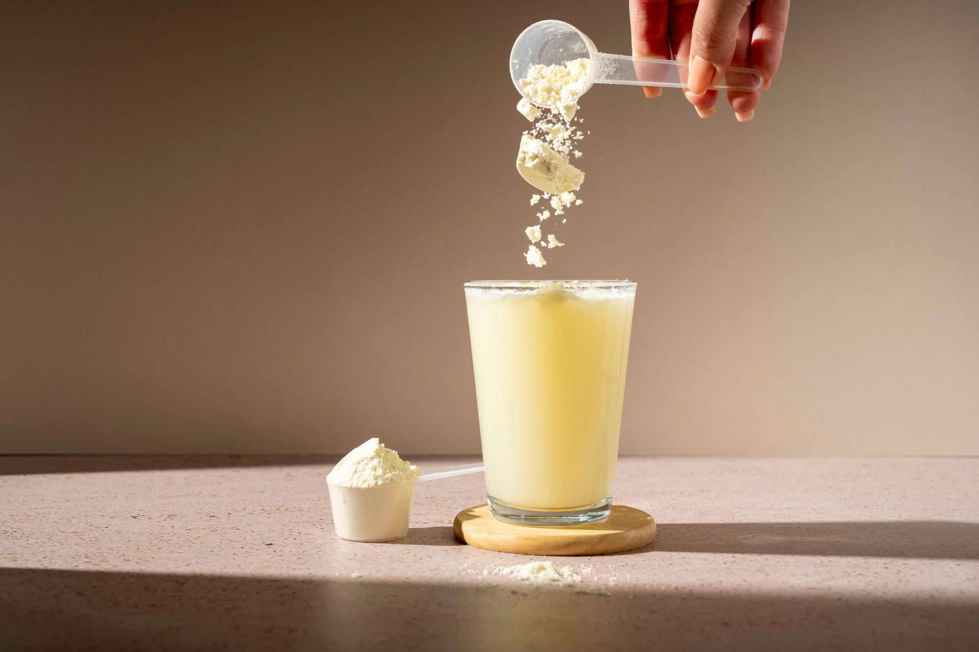 Eine Person schüttet Proteinpulver in ein Glas Milch.