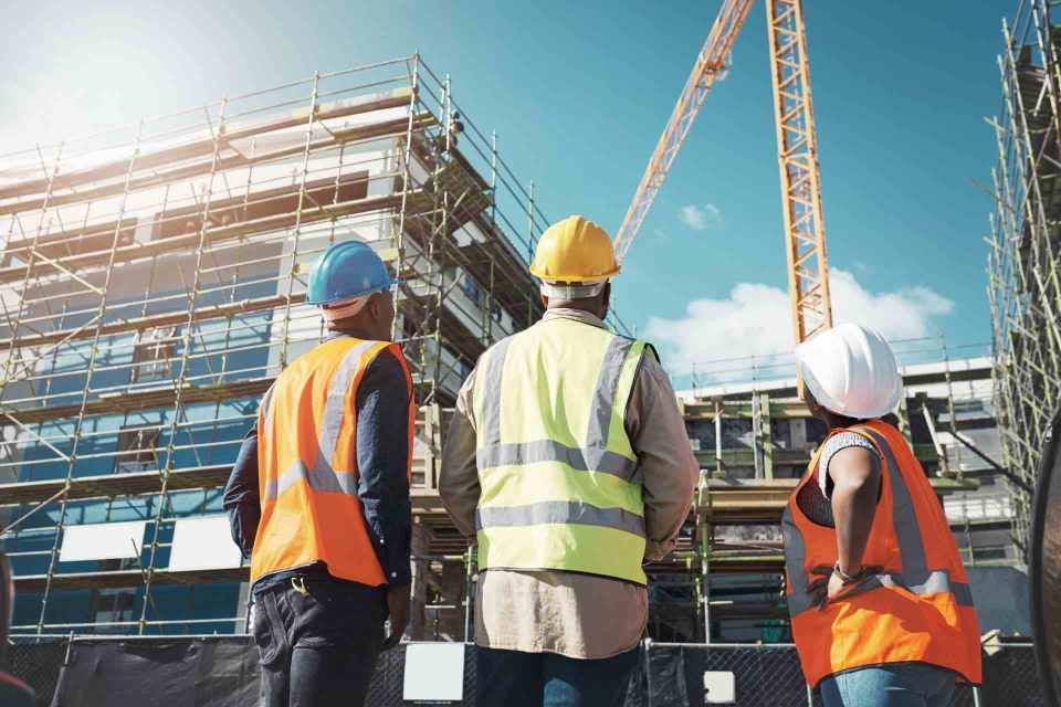 Eine Gruppe Bauarbeiter steht vor einem im Bau befindlichen Gebäude.