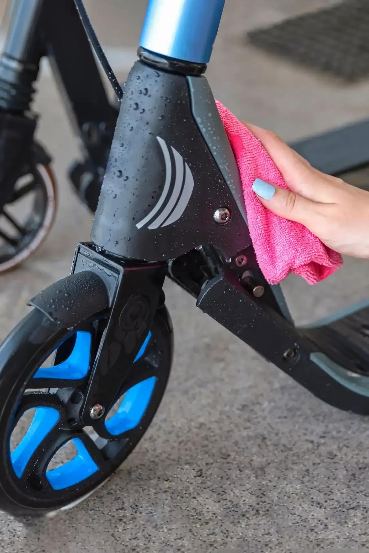 La mano de una persona limpiando gotas de agua de un scooter negro con detalles azules y un paño rosa.