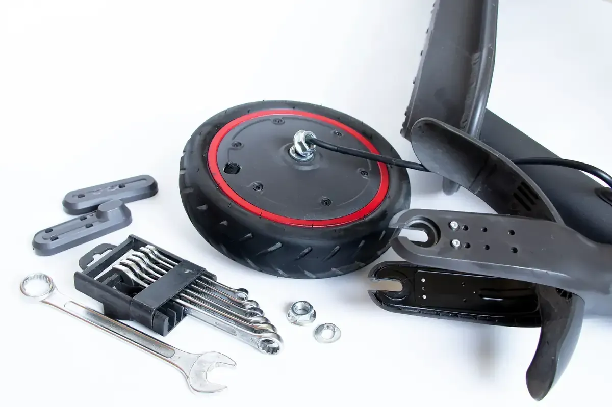 Rueda de scooter y piezas dispuestas con herramientas, incluidas llaves inglesas y llaves Allen sobre una superficie blanca.