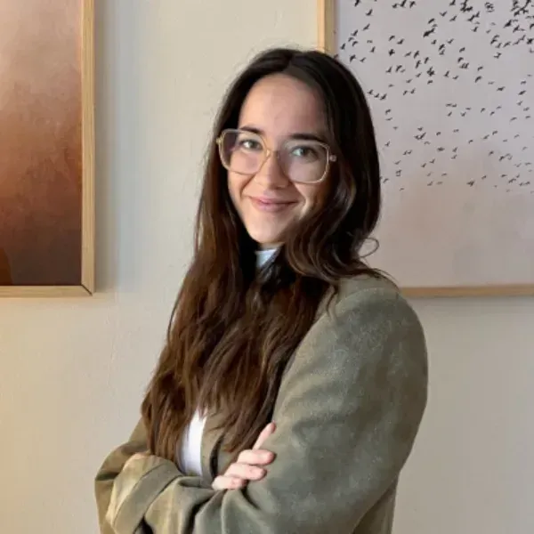 Persona sonriente con gafas y brazos cruzados, de pie en el interior de una vivienda junto a un cuadro enmarcado.