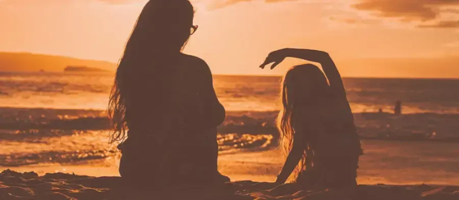Silhouettes of two people on a beach at sunset, one standing and one leaning backward against orange sky.