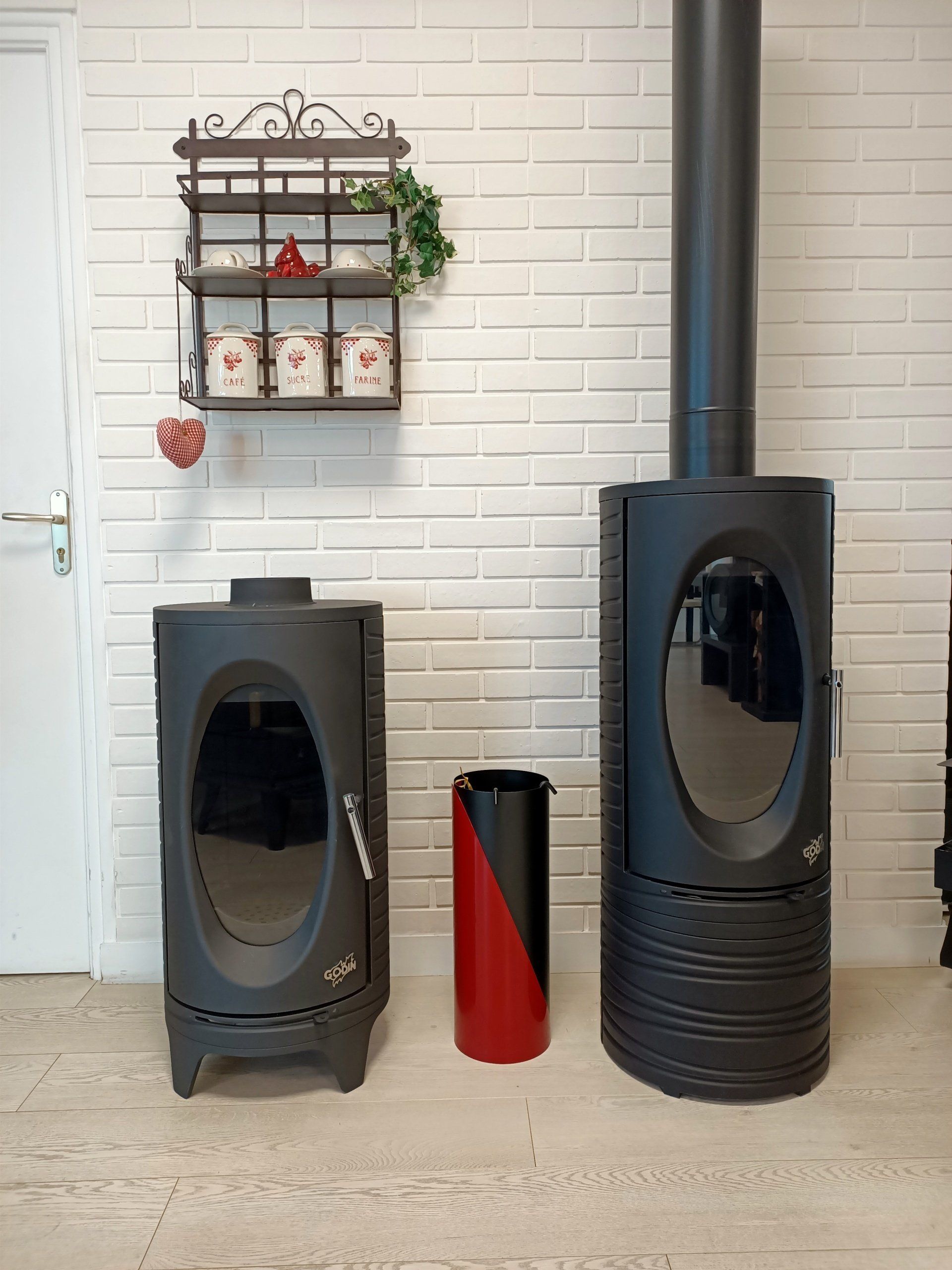 Deux poêles à bois noirs, un vase et une étagère sur un mur de briques blanches