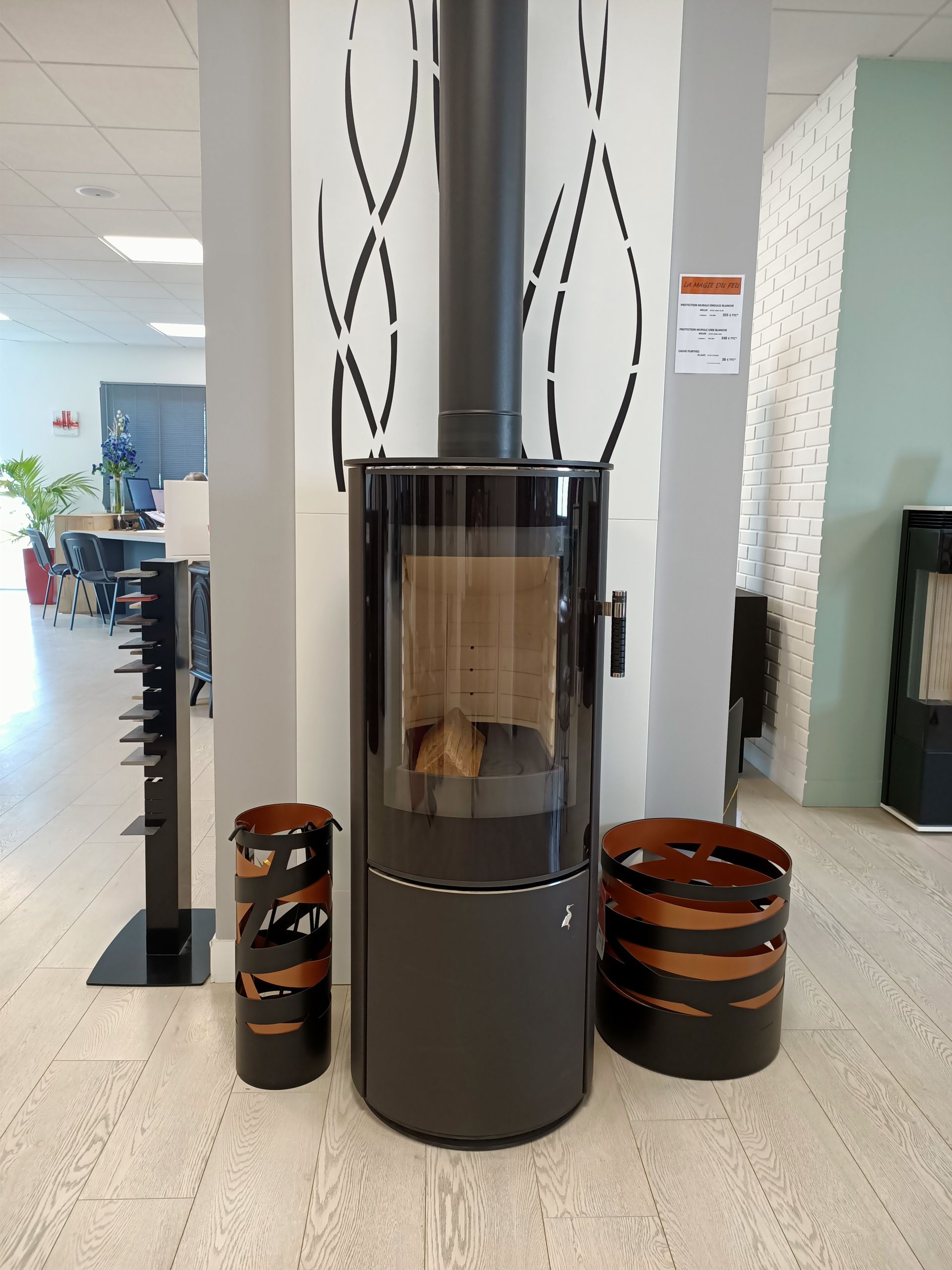 Poêle à bois cylindrique gris foncé avec façade en verre transparent, flanqué de deux récipients métalliques décoratifs.