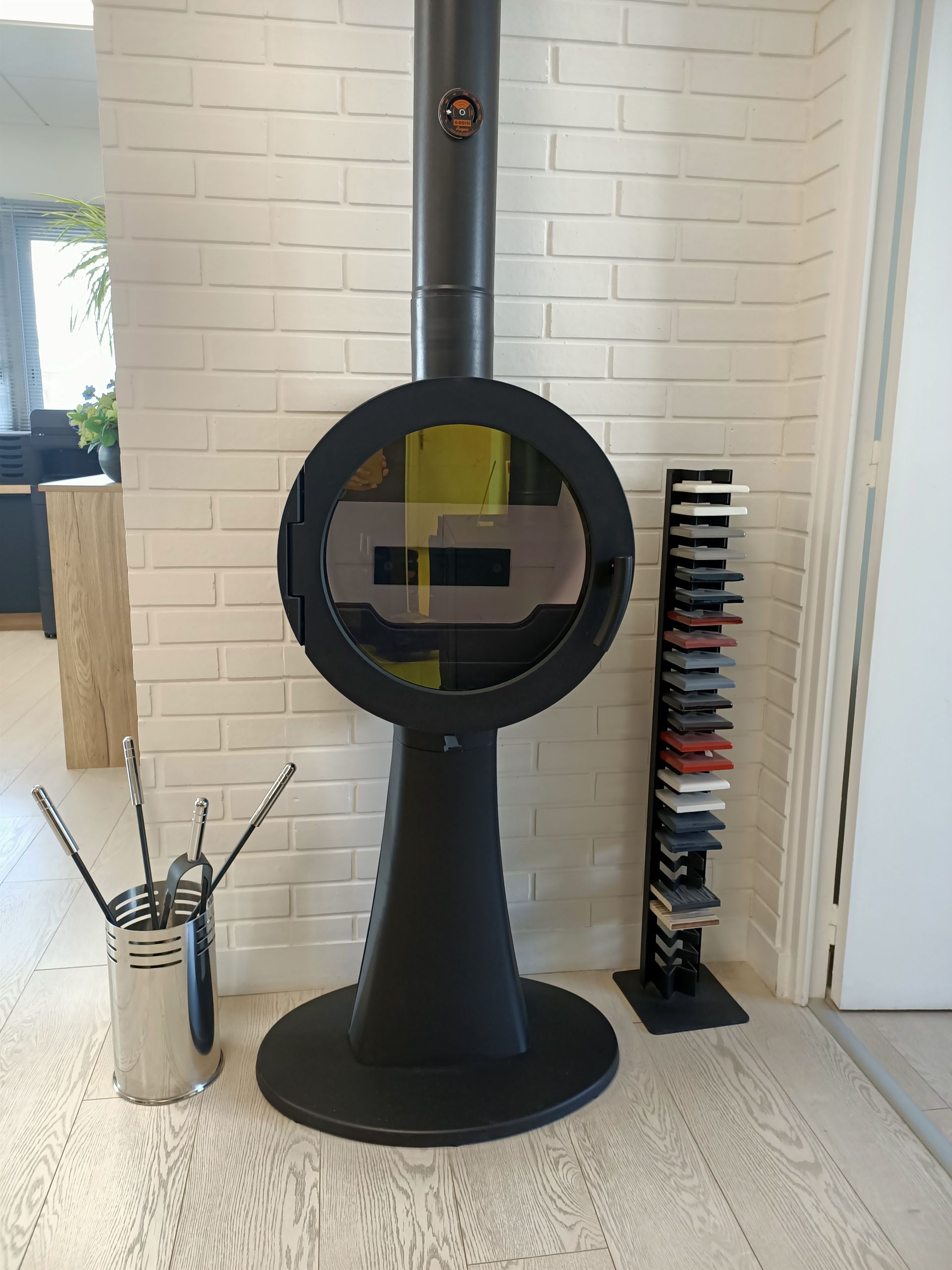 Cheminée moderne noire avec vitre circulaire, contre un mur de briques blanches