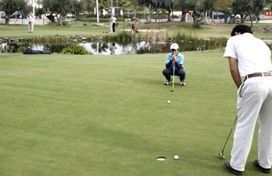 Un hombre está metiendo una pelota de golf en un hoyo en un campo de golf.