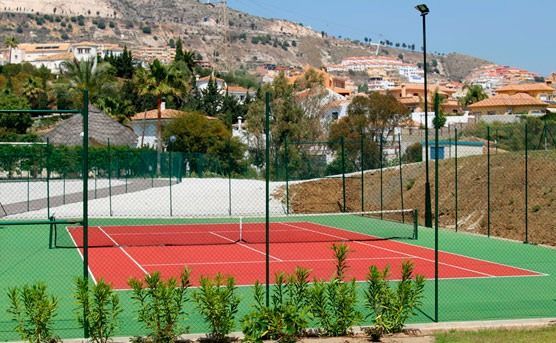Una cancha de tenis roja y verde con una valla alrededor.