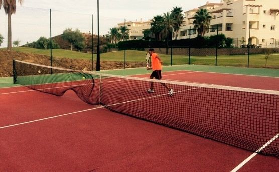 Un hombre está jugando al tenis en una cancha de tenis roja.