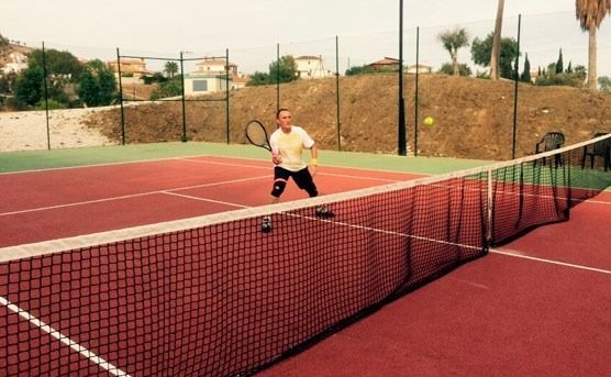 Un hombre está jugando al tenis en una cancha roja.