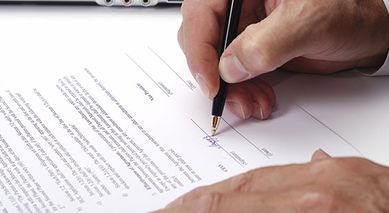 Firma a mano de un documento con bolígrafo sobre un escritorio blanco.