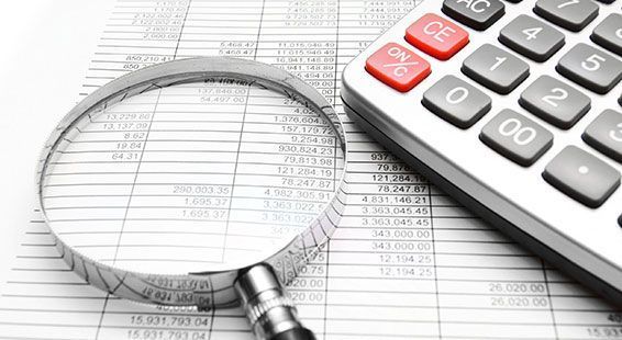 Lupa sobre una hoja de cálculo financiera junto a una calculadora, lo que sugiere contabilidad o análisis de datos.