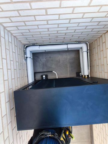 Vista cenital de una caja negra de servicios y tuberías blancas dentro de un estrecho conducto alicatado.