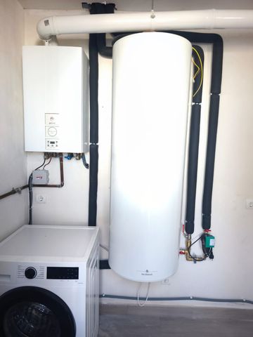 Lavadero con un depósito de agua caliente blanco, una unidad montada en la pared y una lavadora debajo de las tuberías