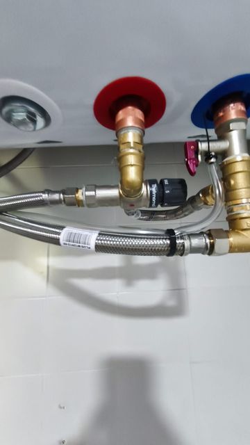 Primer plano de las tuberías debajo del fregadero, con válvulas de agua rojas y azules y mangueras trenzadas