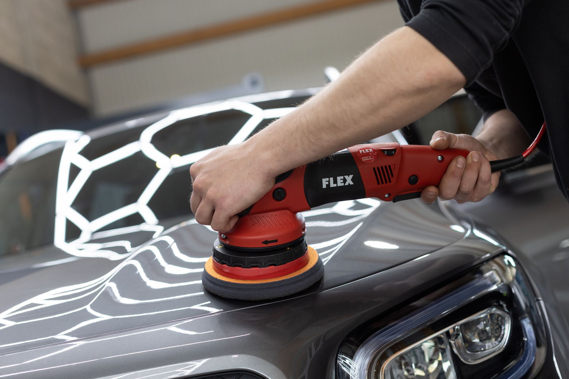 Ein Mann poliert die Motorhaube eines Autos mit einer Maschine.