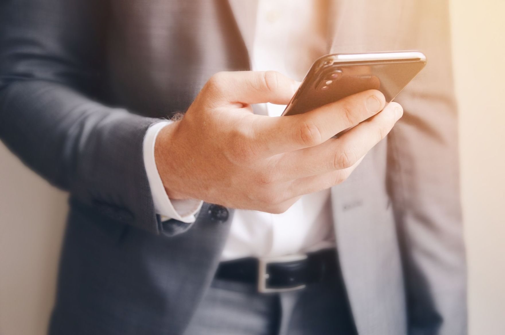 Une personne en costume gris tenant un smartphone et regardant l'écran.