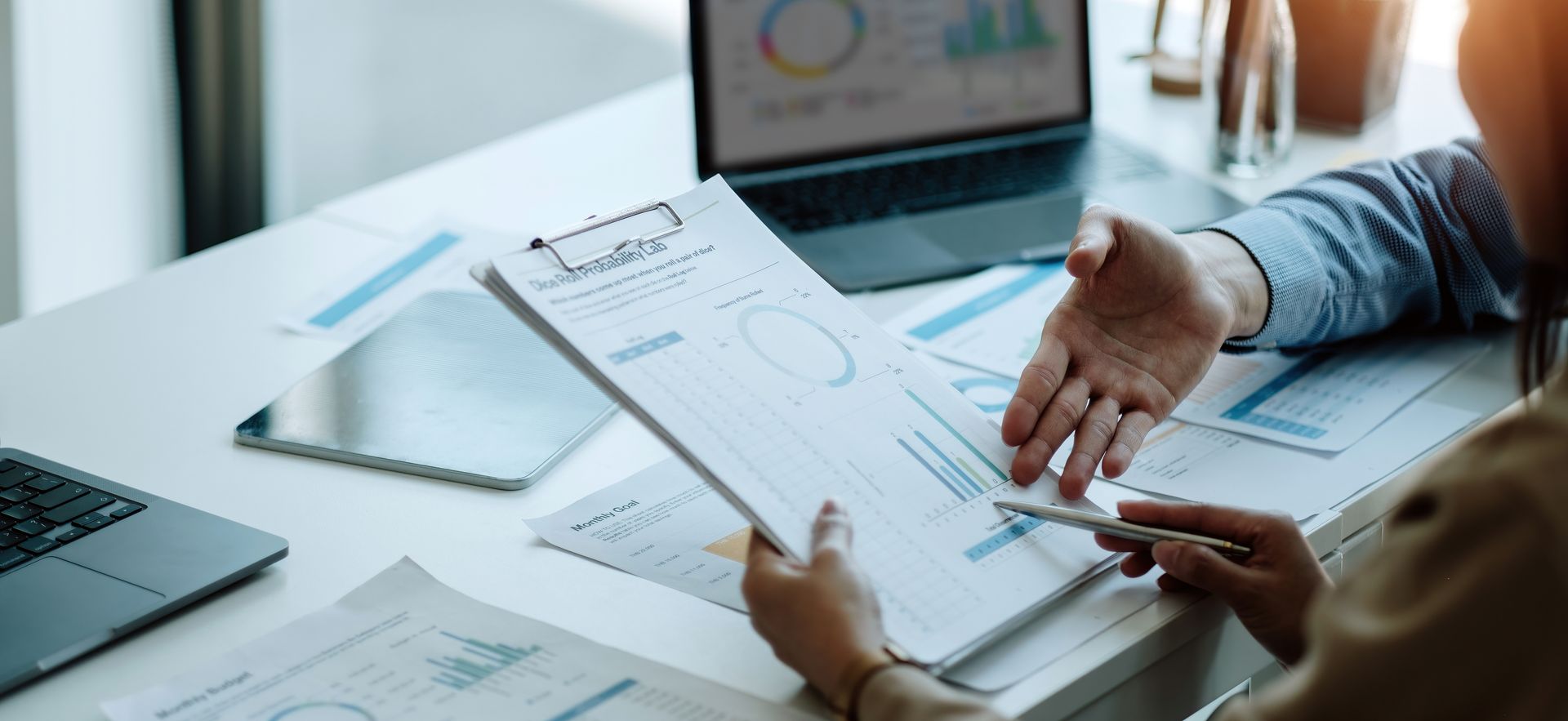 Deux collègues analysent des graphiques et des données commerciales sur des documents lors d'une réunion à un bureau équipé d'ordinateurs portables.