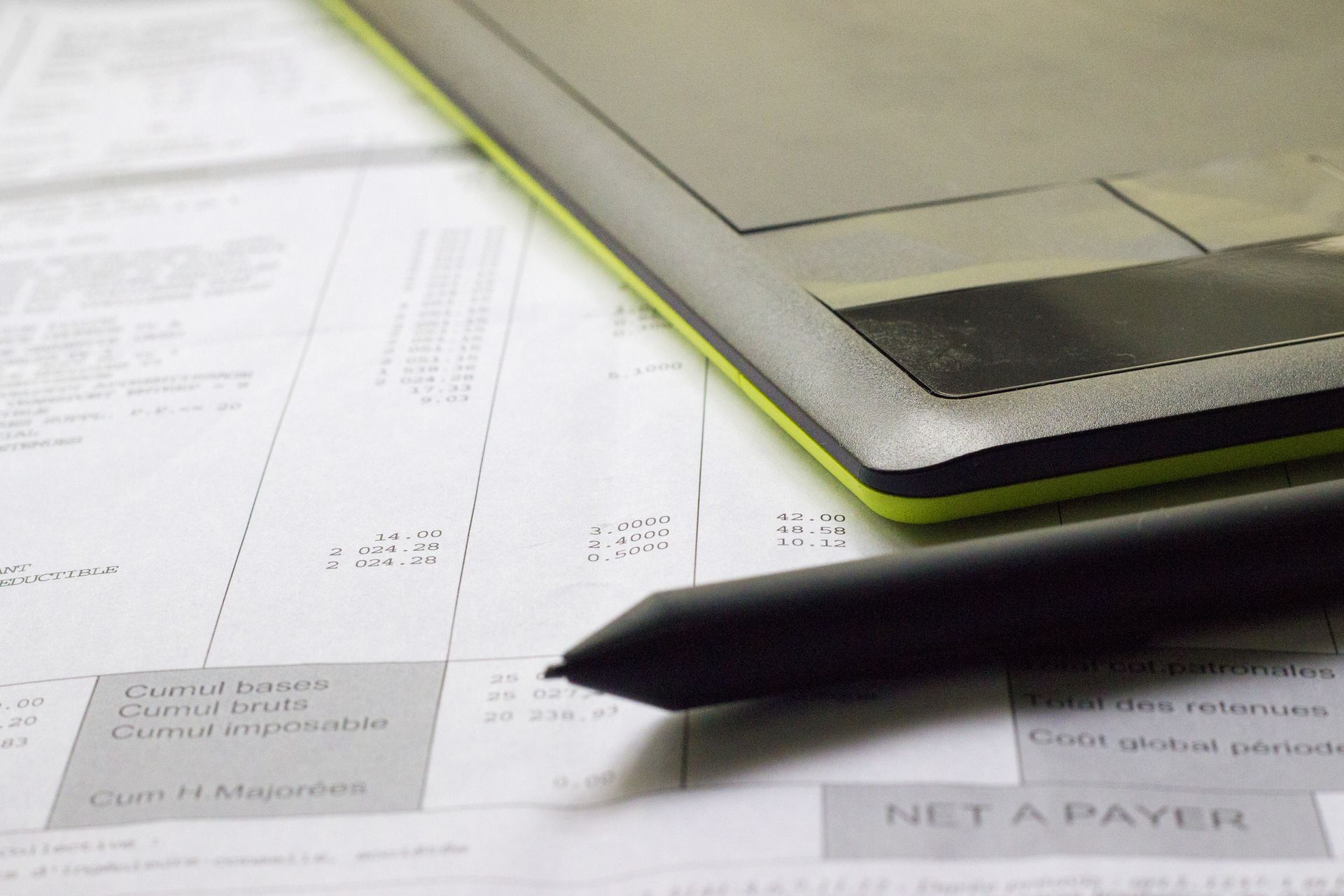Une tablette graphique et un stylet posés sur un document financier imprimé comportant une section visible NET A PAYER.