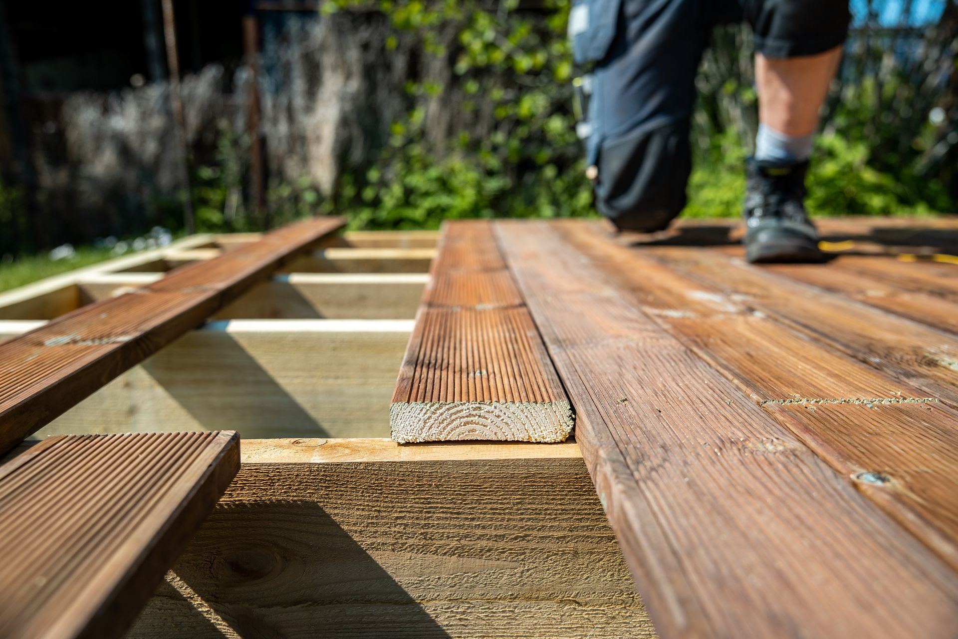 Charpente de terrasse en bois en construction, avec les bottes d'un ouvrier visibles en arrière-plan.