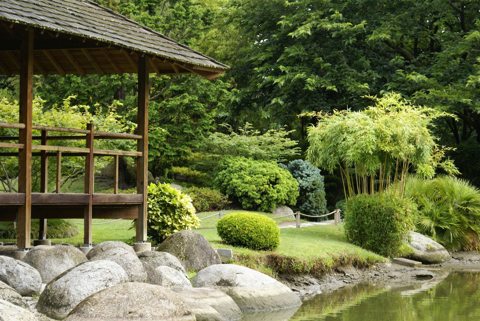 Jardin japonais avec un pavillon en bois, des rochers et une végétation luxuriante au bord d'un étang