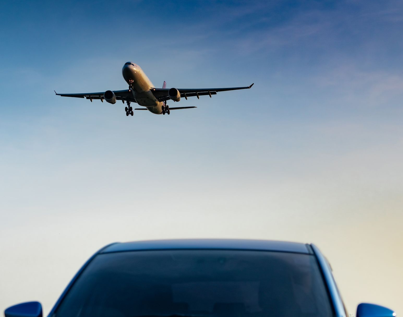 Véhicule en premier plan avec un avion dans le ciel derrière