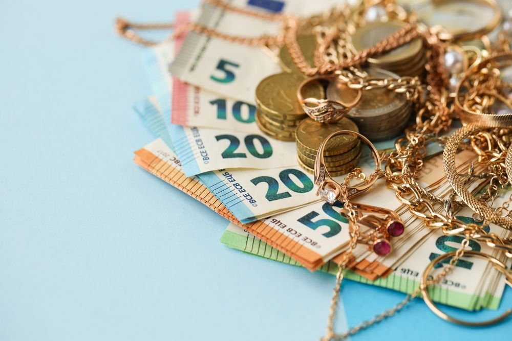 Una pila de billetes de euro de distintas denominaciones, coronada con un montón de monedas de oro