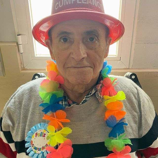 Un hombre mayor que lleva un sombrero rojo y flores alrededor del cuello.