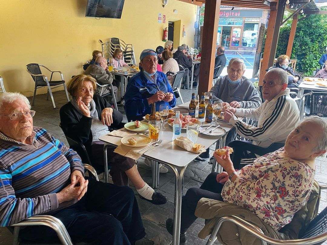 Un grupo de personas mayores están sentadas alrededor de una mesa comiendo comida.