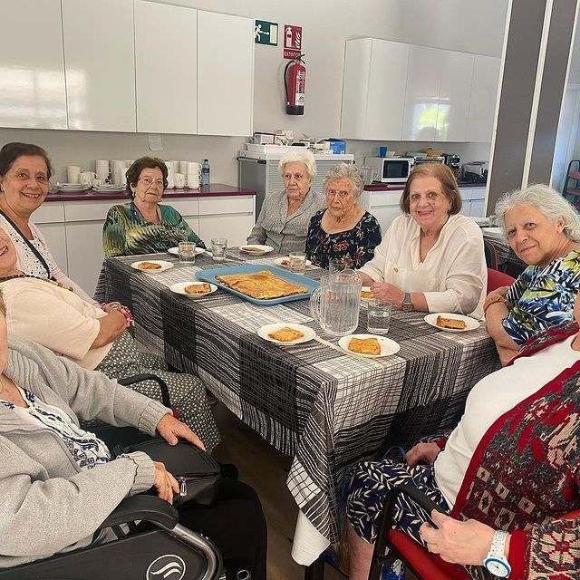 Un grupo de mujeres mayores están sentadas alrededor de una mesa comiendo comida.
