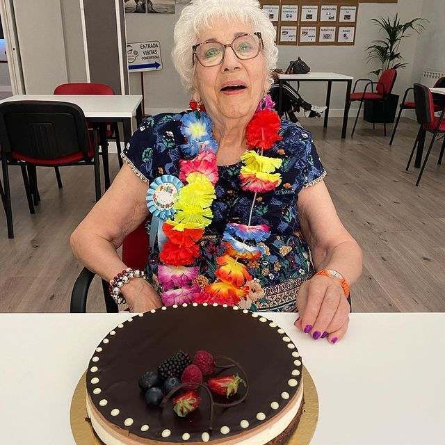 Una mujer mayor está sentada en una mesa con un pastel encima.