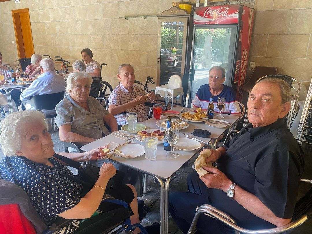 Un grupo de personas mayores están sentadas en mesas comiendo comida.
