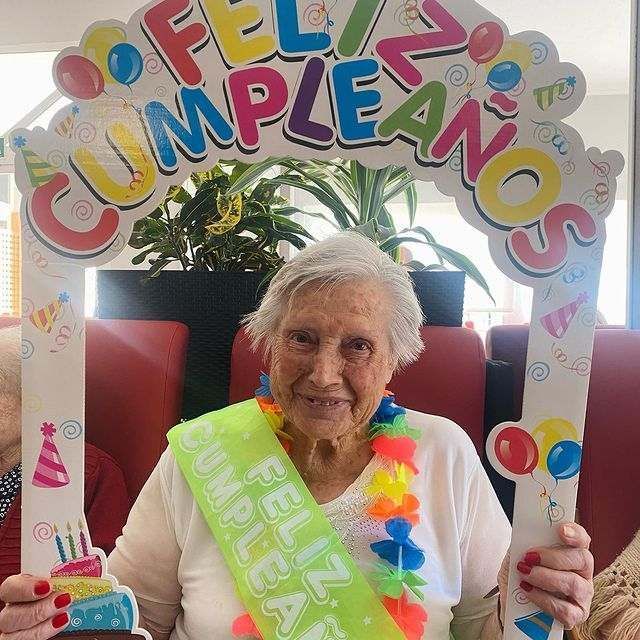 Una mujer mayor sostiene un cartel que dice feliz cumpleaños