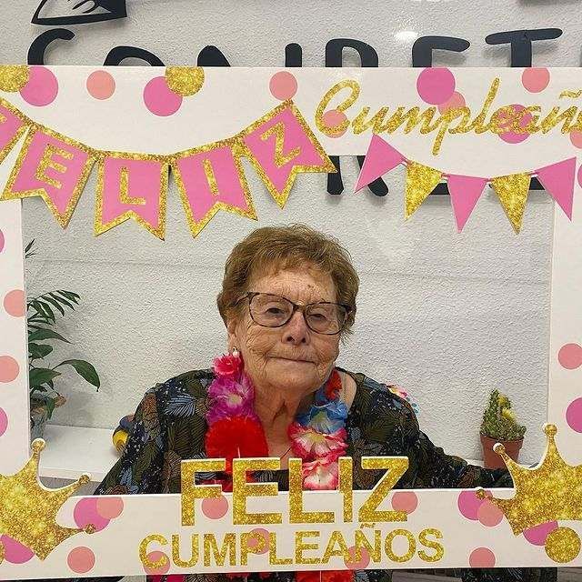 Una mujer mayor posa para una foto con un marco que dice feliz cumpleaños