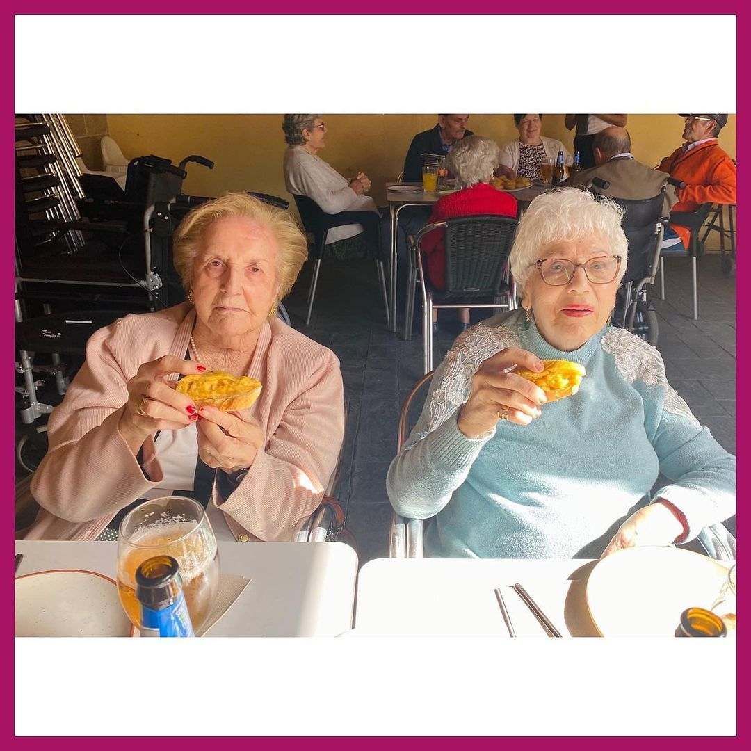 Dos mujeres mayores están sentadas en una mesa comiendo comida.