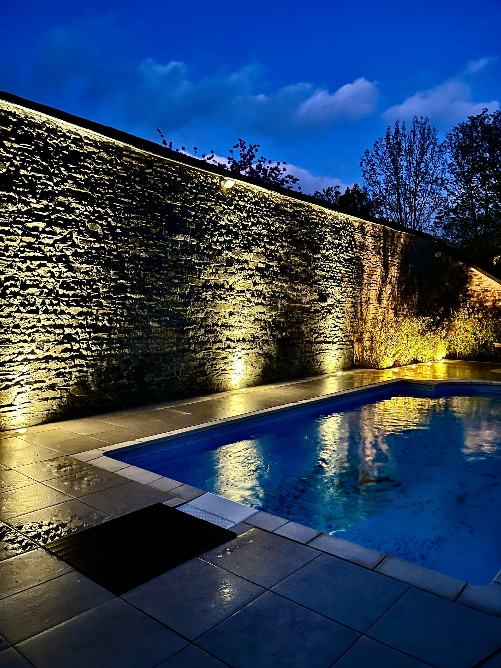 Piscine et mur en pierre vus de nuit
