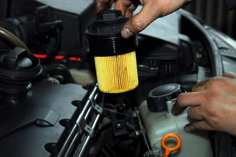Una persona sostiene un filtro amarillo delante del motor de un automóvil.