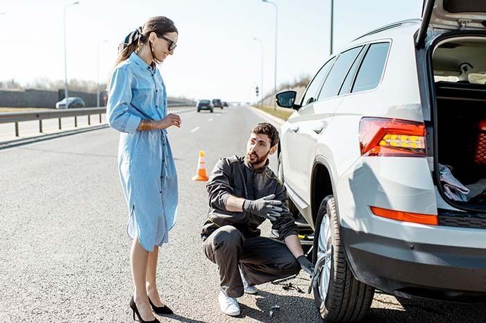 Un hombre está cambiando una llanta de un automóvil mientras una mujer observa.