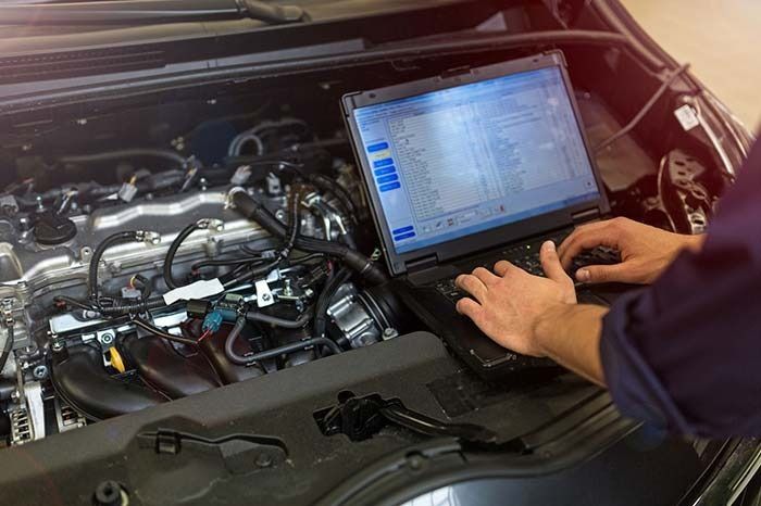 Un mecánico está usando una computadora portátil para revisar el motor de un automóvil.