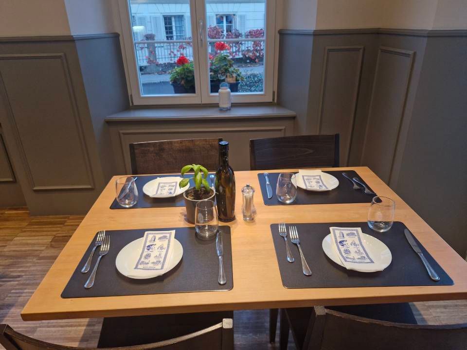 Ein für vier Personen gedeckter Restauranttisch mit Tellern, Besteck und einer Weinflasche.